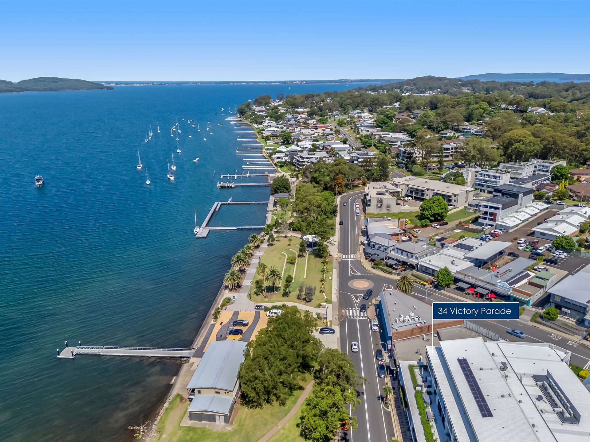 Aerial view of a coastal town with blue water, docks, roads, and buildings along the shoreline.