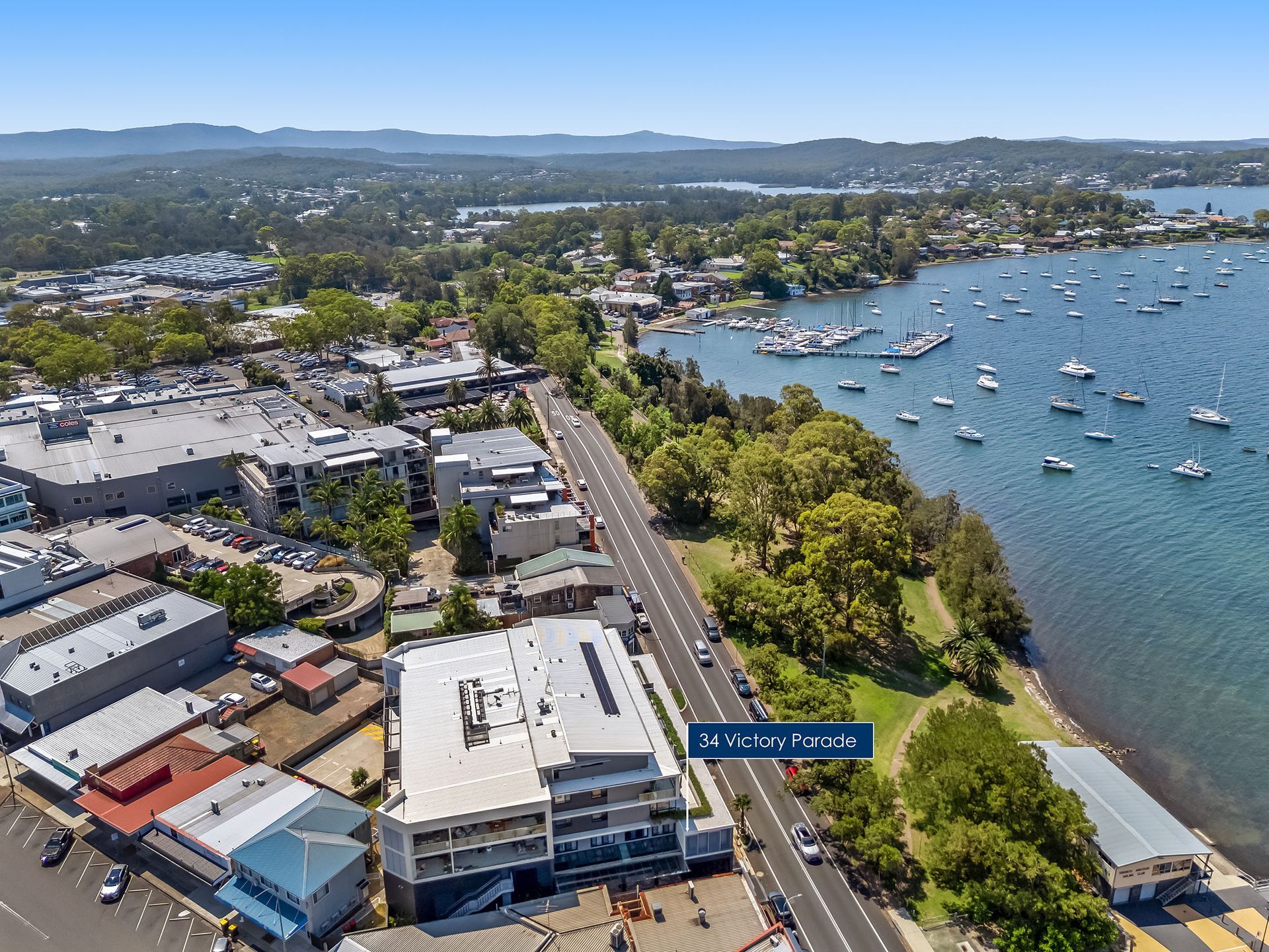 Aerial view of a coastal town with boats in a bay, roads, buildings, and tree-lined shoreline