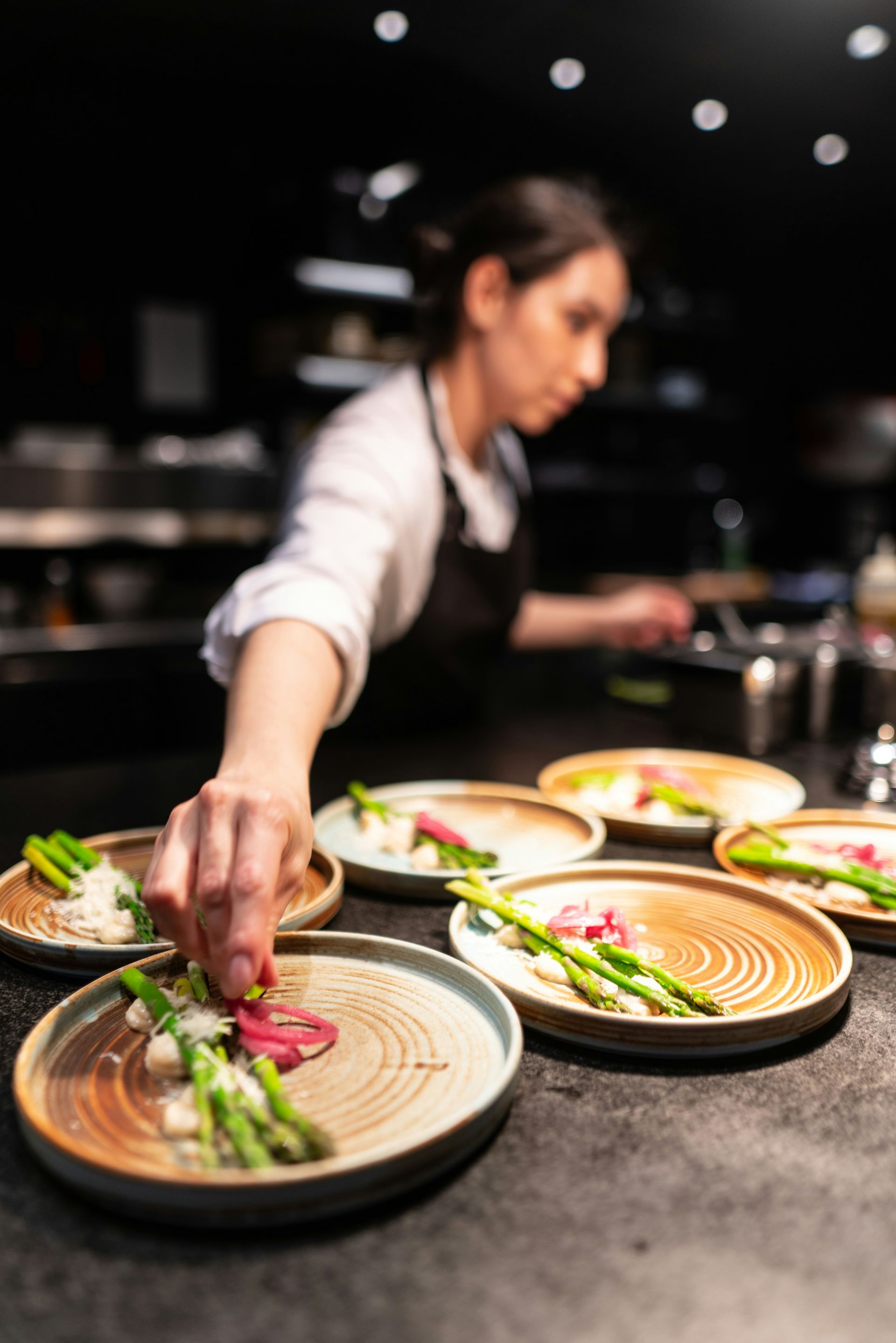 Chef plating colorful dishes on a counter in a dimly lit restaurant kitchen