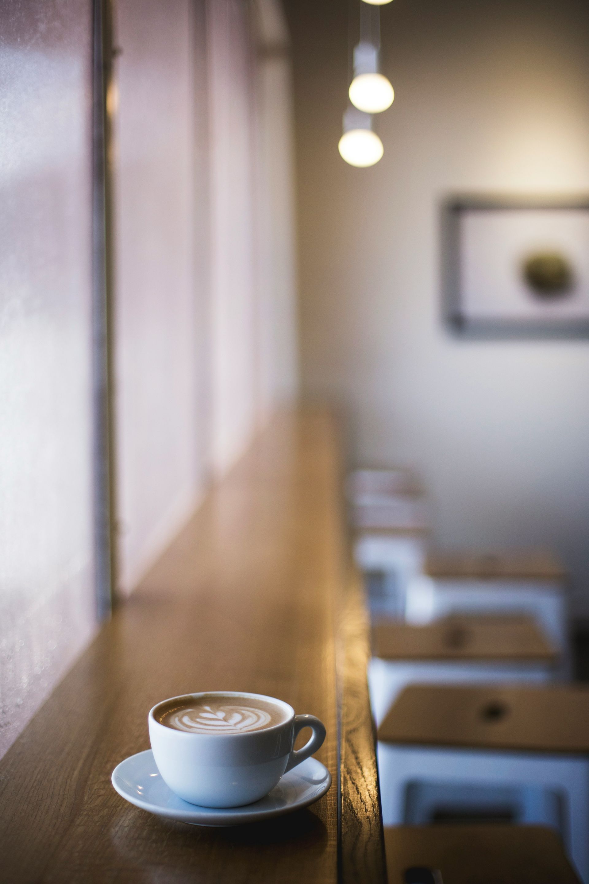 White coffee cup and saucer on a wooden counter in a softly lit cafe interior.