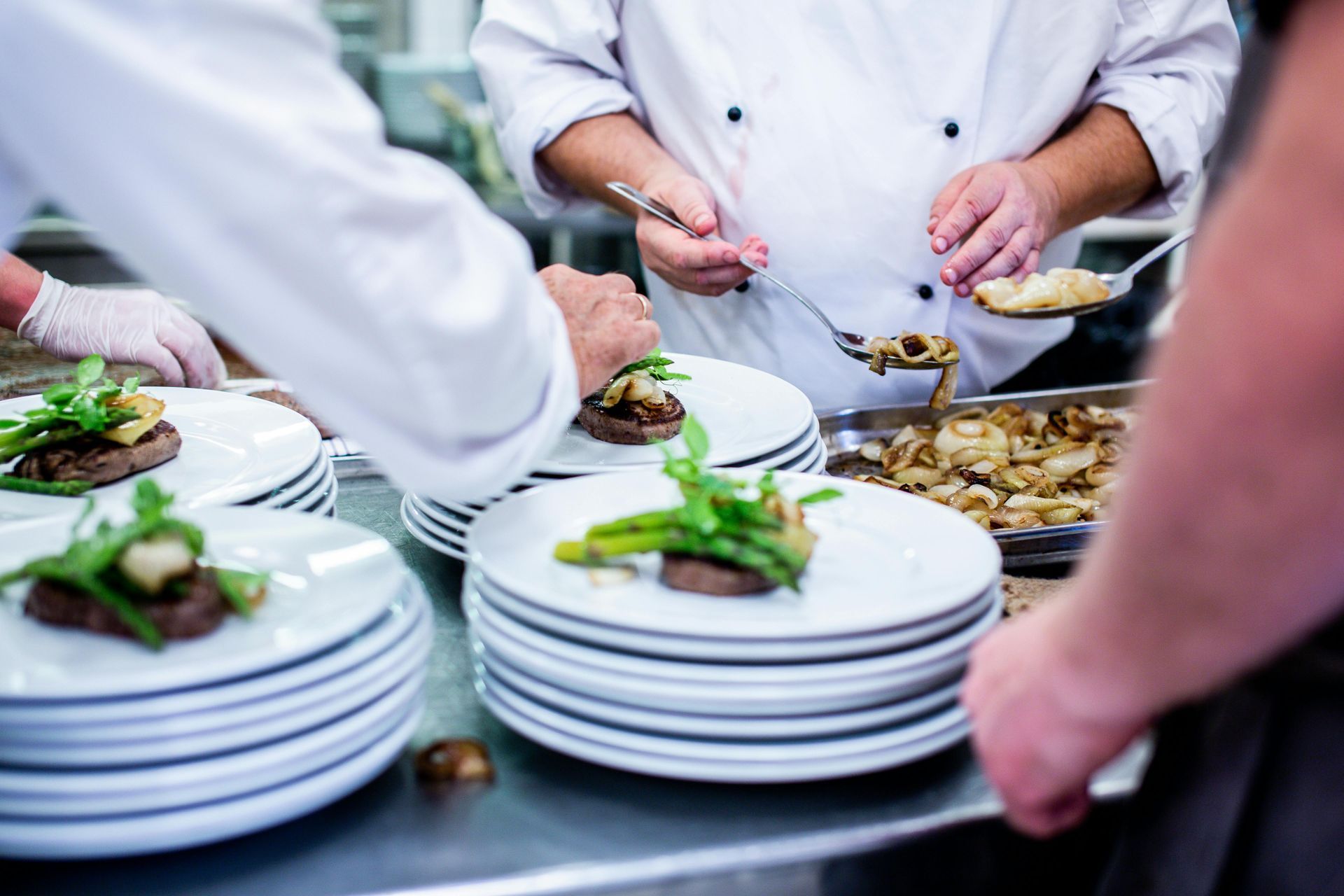 Chefs plating garnished dishes on stacked white plates at a catering buffet
