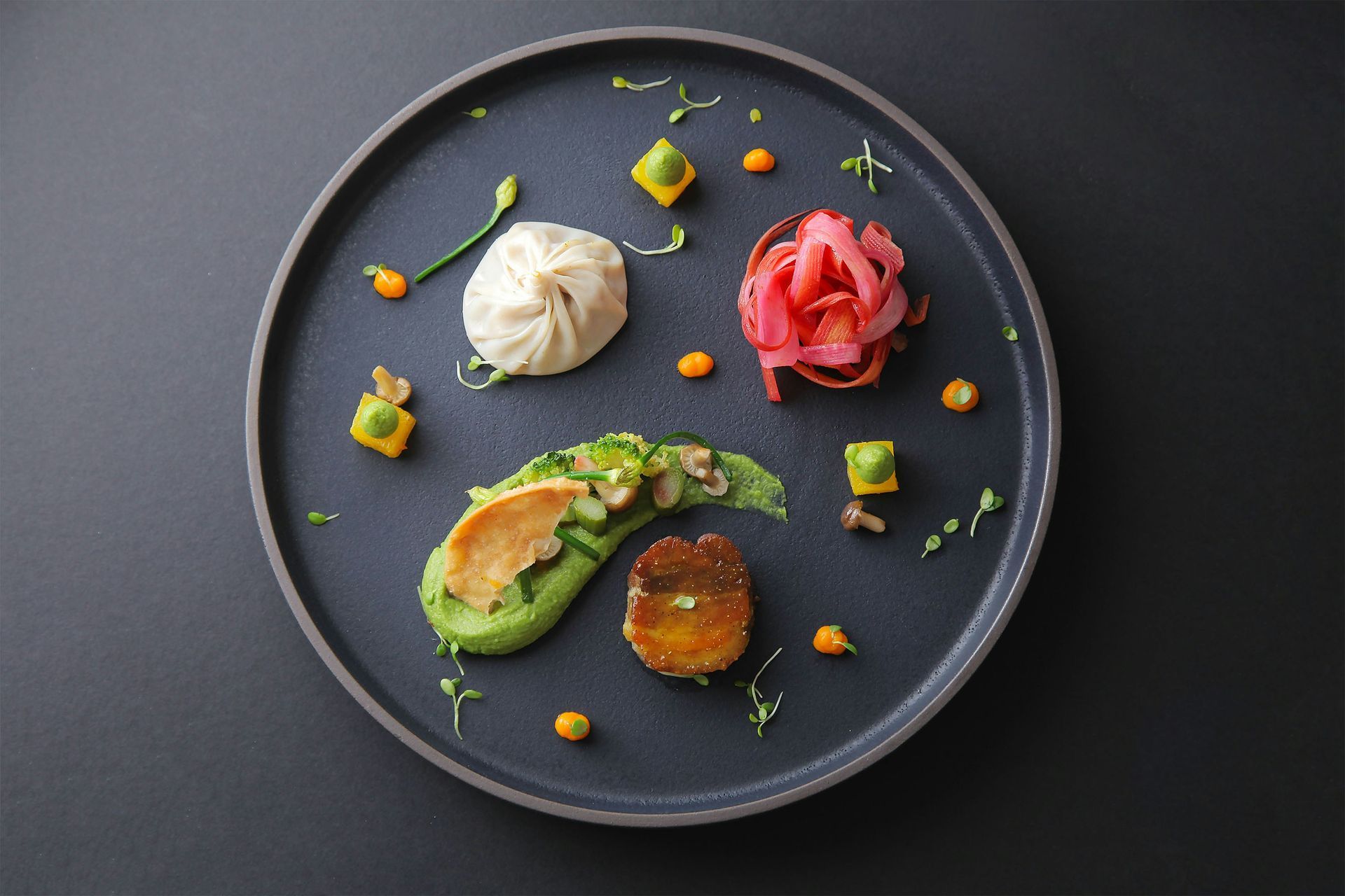 Elegant plated gourmet dish with avocado, poached egg, and beet garnish on a dark round plate