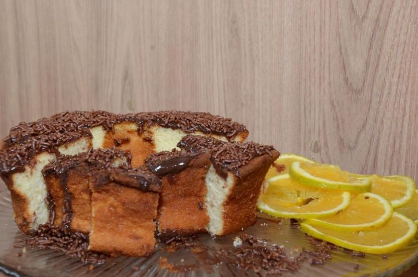 Bolo com cobertura de chocolate e recheio cremoso, fatiado para mostrar o interior, ao lado de fatias de limão em um prato.