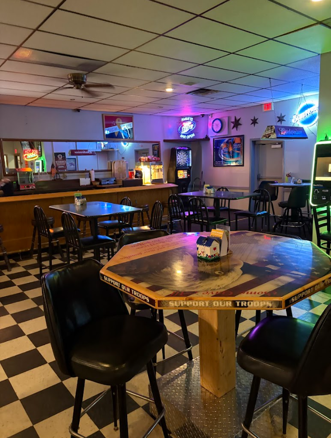 Dimly lit bar interior with checkered floor, wooden tables, neon lights, and a wall-mounted TV near the counter