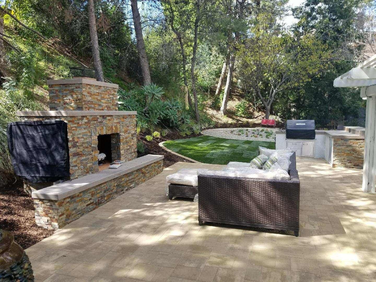 Outdoor living space with stone fireplace, seating, and grill.