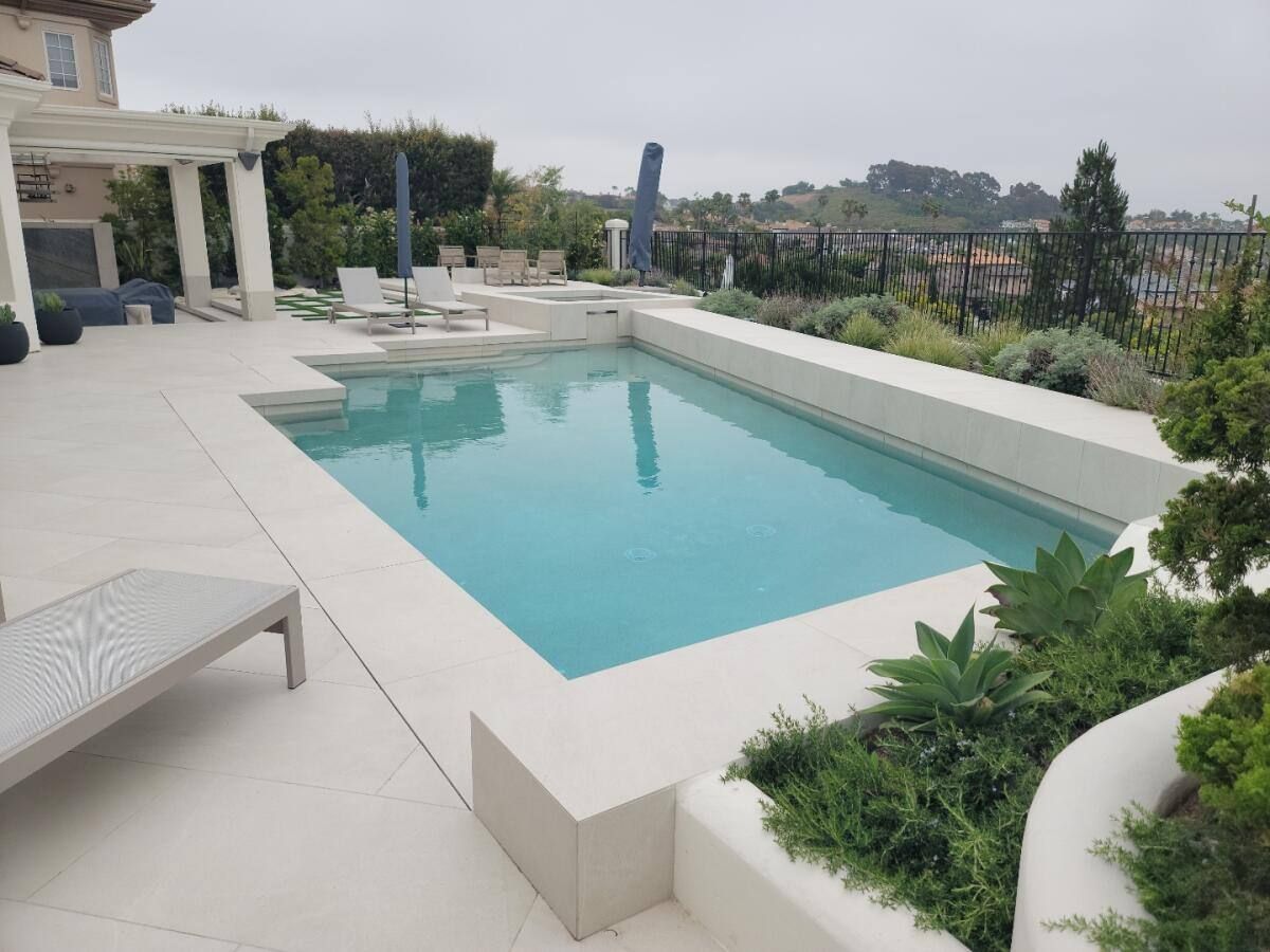 Rectangular pool with white stone surround, landscaping, and view of distant buildings.