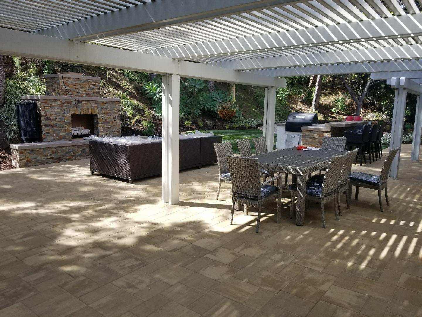 Patio with pergola, fireplace, dining set, and grill; neutral tones; outdoor setting.