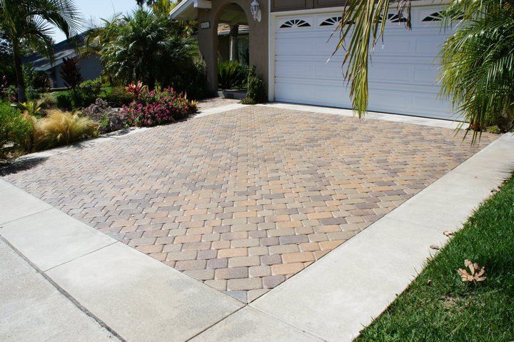 Brick driveway in front of a garage, bordered by concrete and grass.