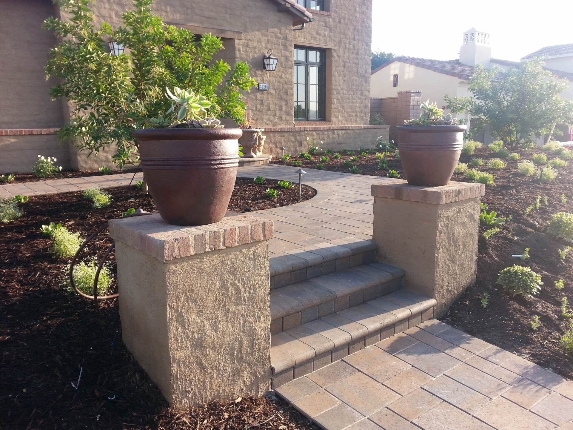 Brick pathway with steps leading to a house, framed by planter boxes and pots.