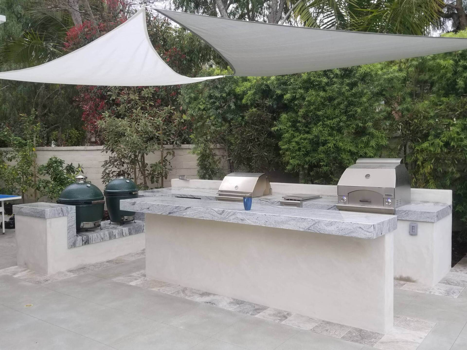 Outdoor kitchen with grills, countertops, and a shade sail.