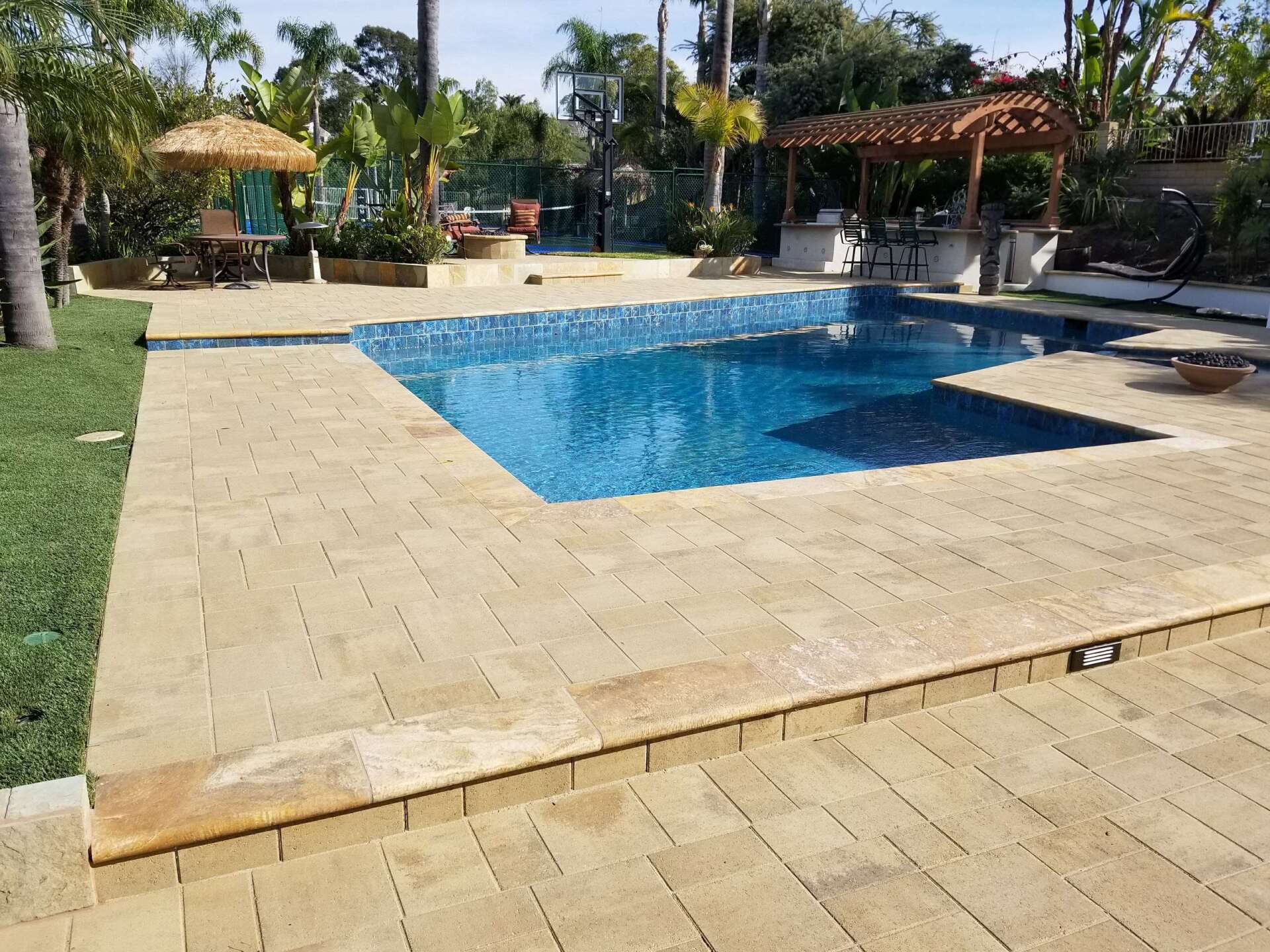 A backyard pool with stone pavers, a bar, and a small seating area on a sunny day.