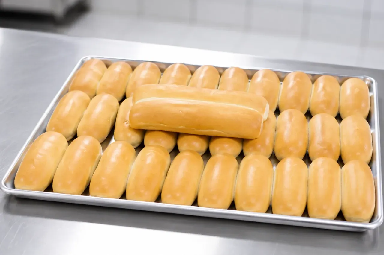 Pan de completo recién horneado en bandeja para producción profesional en panadería.