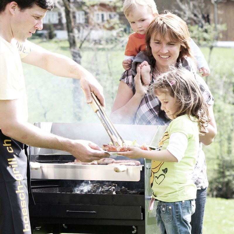 Ein Mann kocht auf einem Grill und eine Frau hält ein Kind