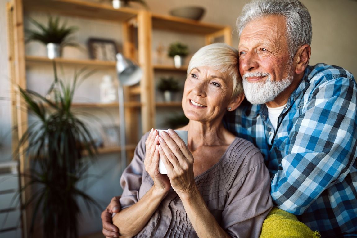 A man and a woman are hugging each other in a living room . the woman is holding a cup of coffee.