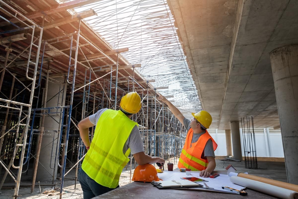 Two builders wearing yellow hardhats and reflectorized vest working on a construction project.