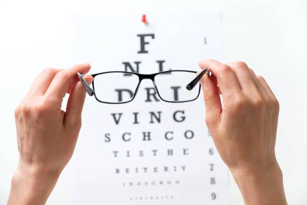 Hands Hold a Pair of Glasses in Front of an Eye Chart — Peninsula Eyecare Izzards Optometrists in Empire Bay, NSW