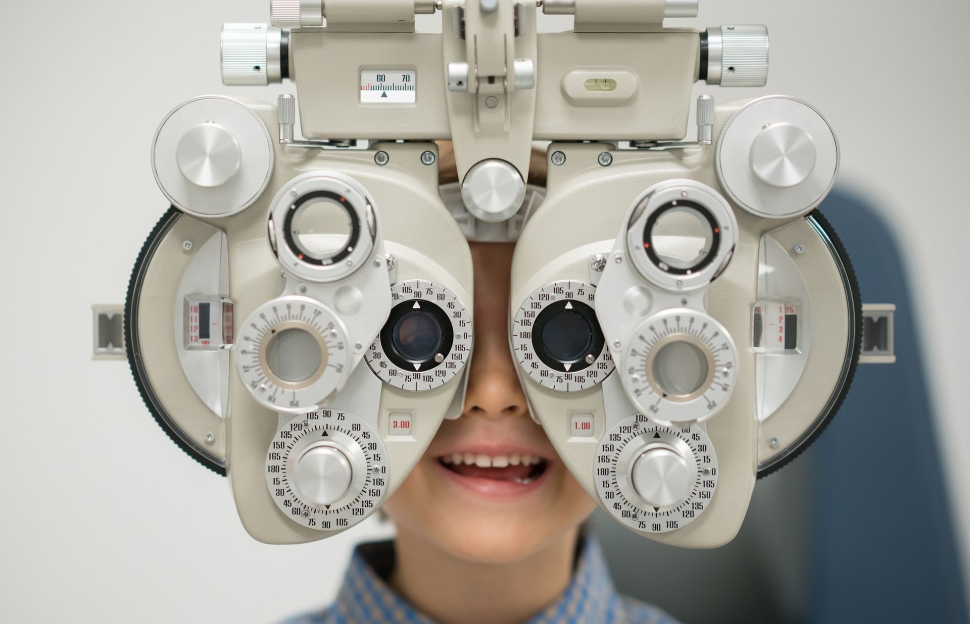 A Child Smiling While Looking Through a Phoropter — Peninsula Eyecare Izzards Optometrists in Point Clare, NSW