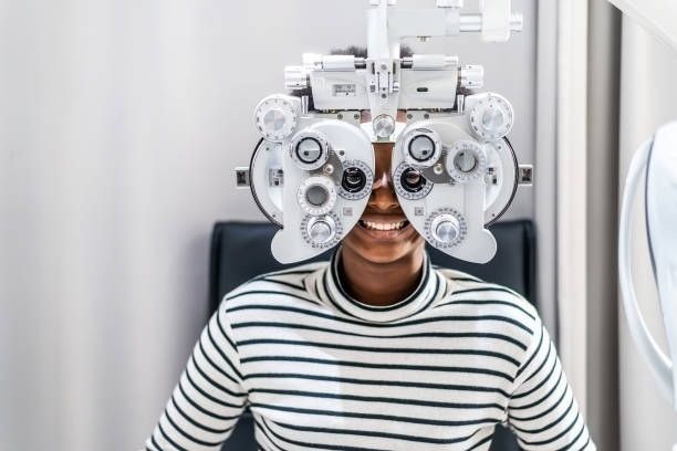 A Person Smiling While Wearing a Phoropter — Peninsula Eyecare Izzards Optometrists in Empire Bay, NSW