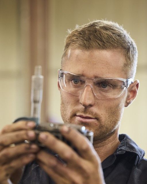 Man in safety goggles examining lab equipment with a tool, focused expression