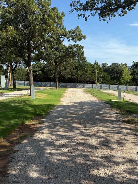 Gravel path through a cemetery with headstones on both sides, trees, and a blue sky.