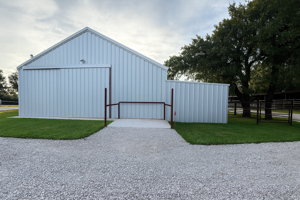 White metal barn with gravel path and green grass under overcast sky.