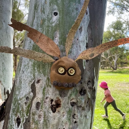 Brown, clay-like creature with leaf wings and twig mouth on tree, with child running in the background.