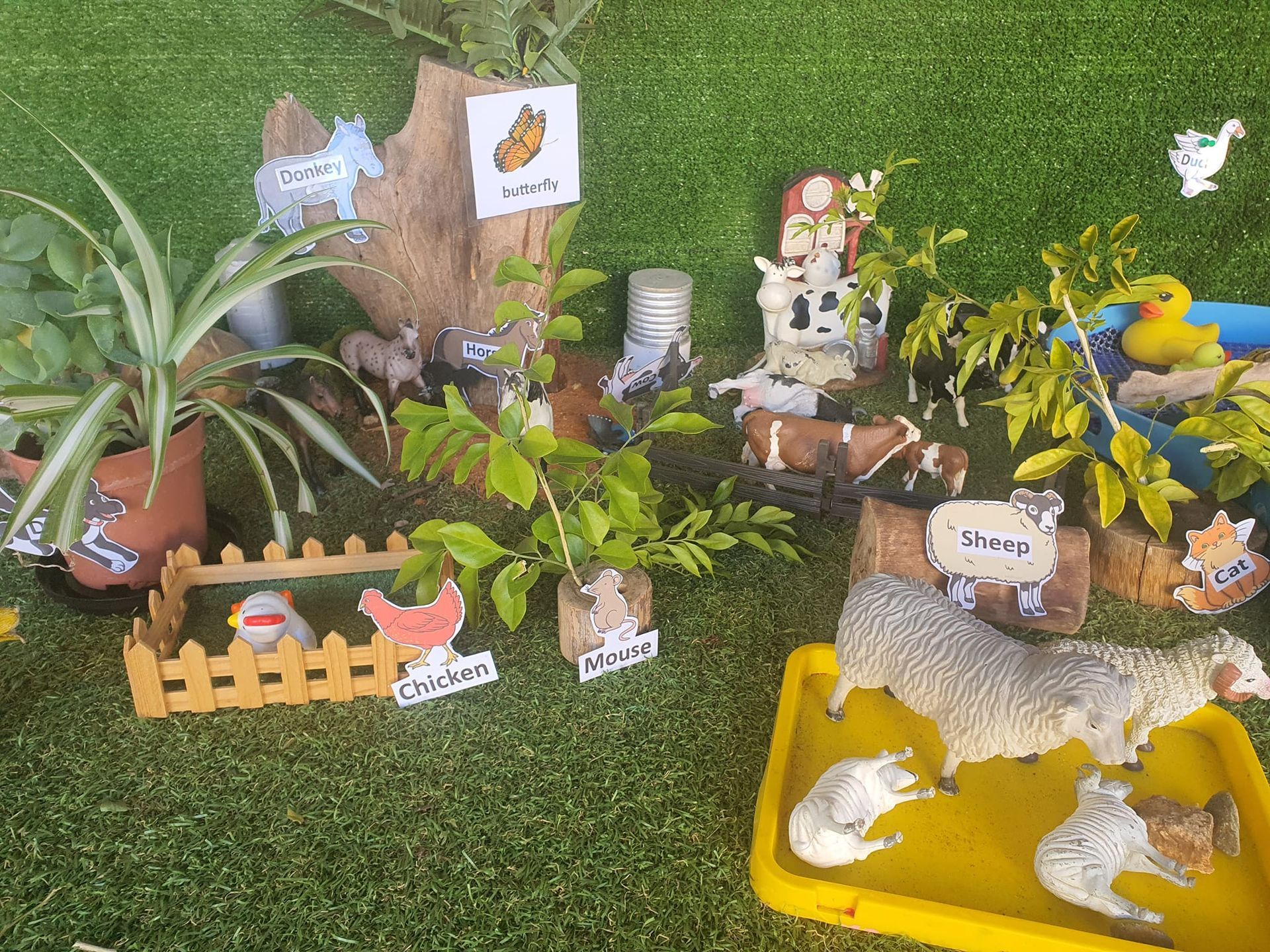 Farm scene with toy animals, plants, and wooden accents on green turf.
