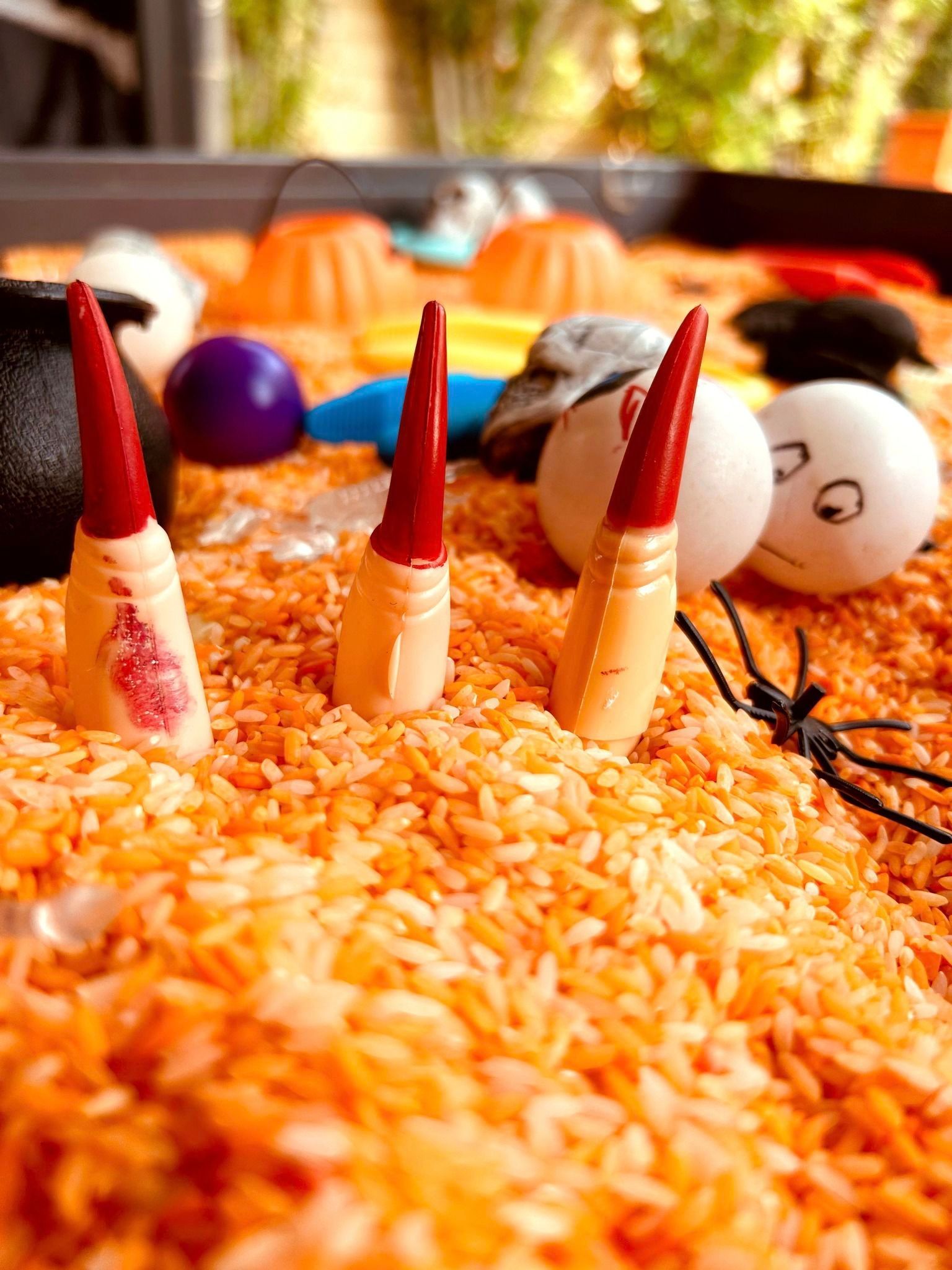 Halloween sensory bin with orange rice, witch fingers, and other decorations.