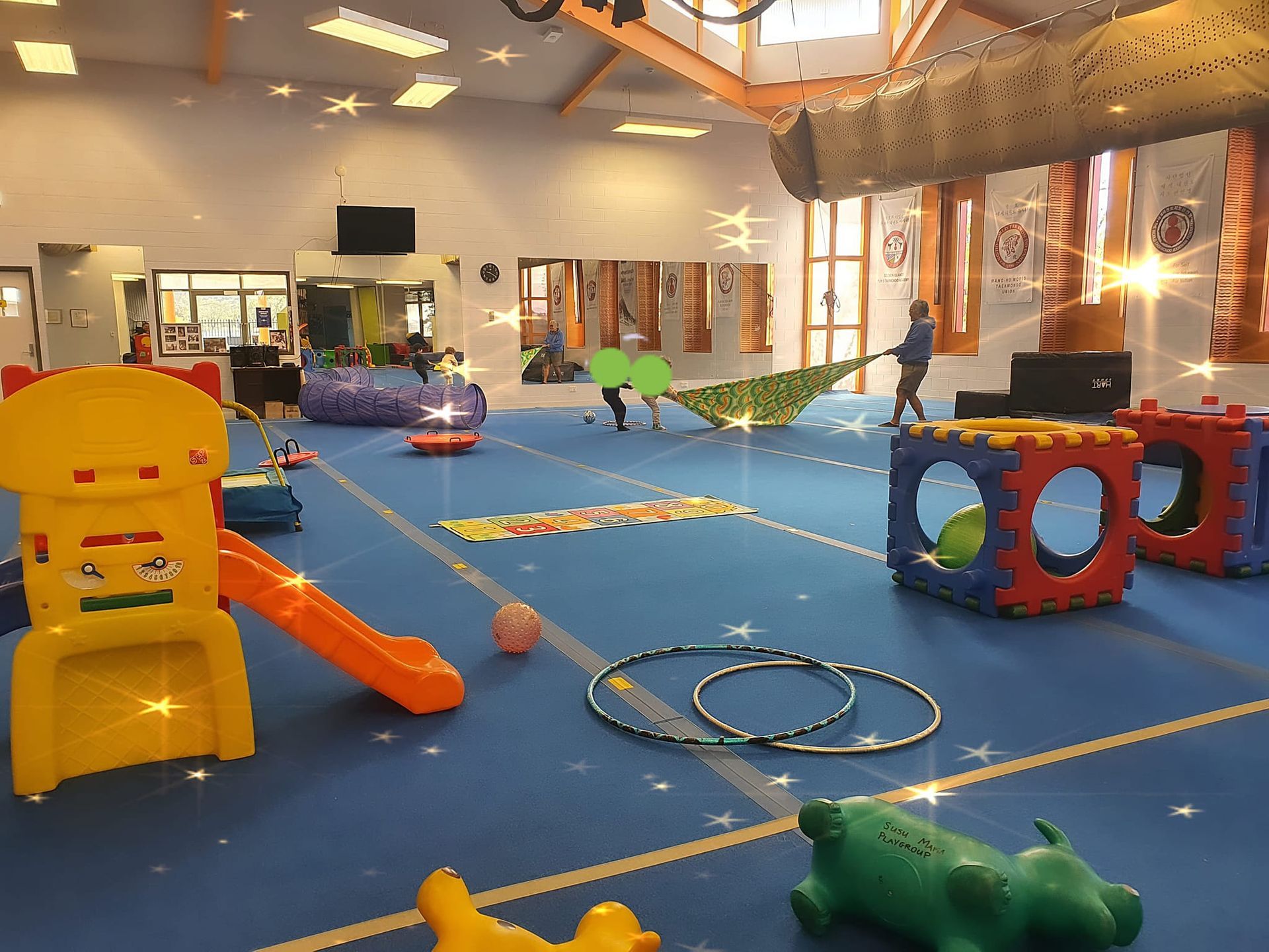 Indoor play space with blue floor, colorful toys, and children playing.