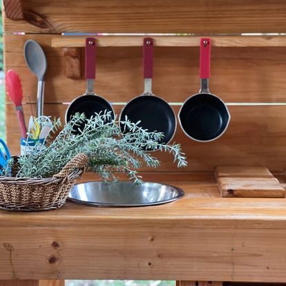 Outdoor play kitchen with pots, utensils, herbs, and a metal basin.