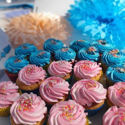 Cupcakes, frosted in pink and blue with sprinkles, arranged in a box with paper flower decorations.