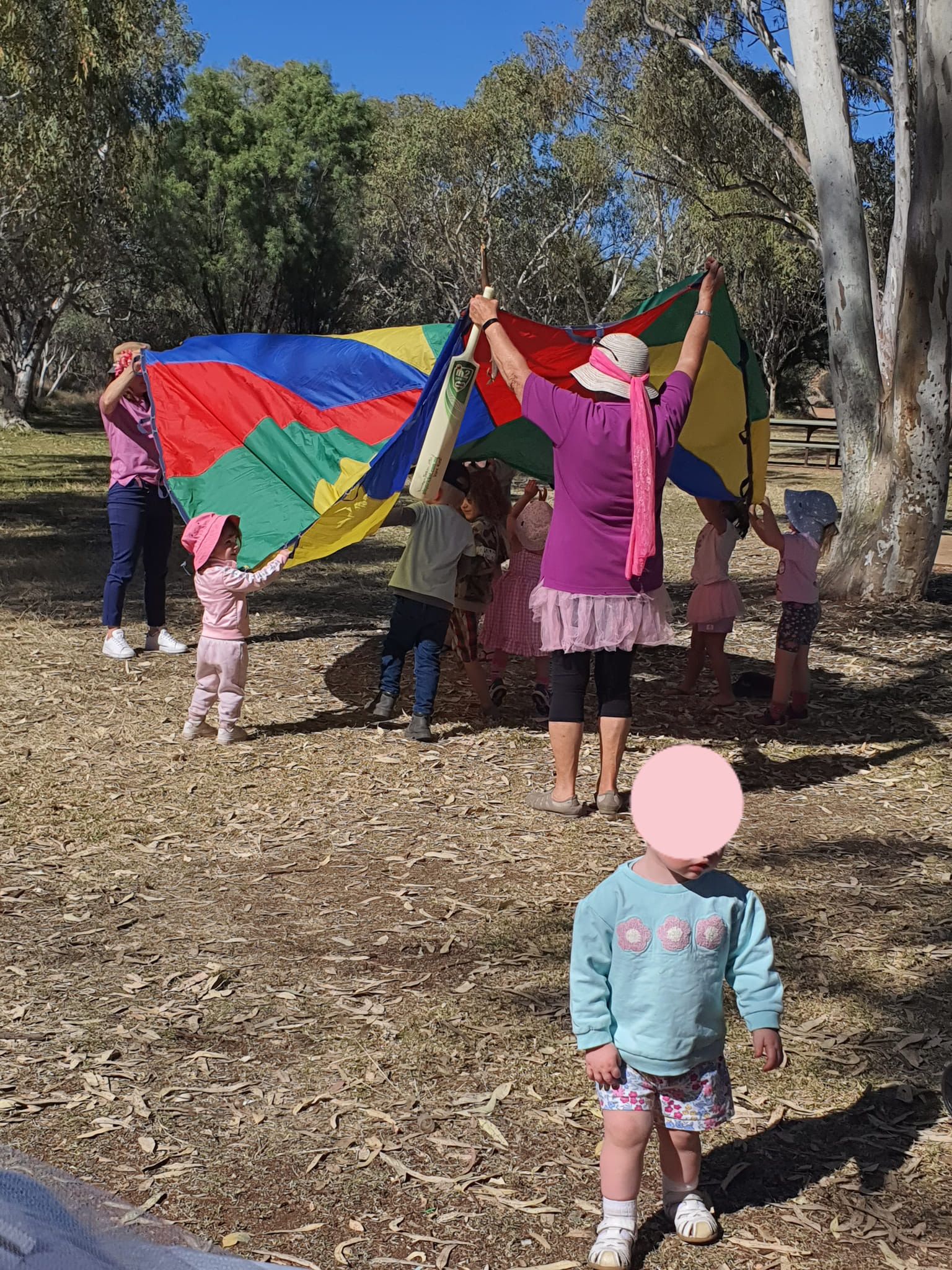 Children and adults play with a colorful parachute outdoors.