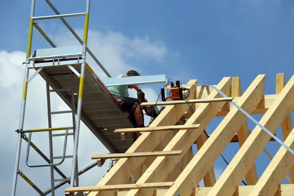 Person on Scaffolding Constructing a Wooden Roof Under a Blue Sky — Wilko Plate (Aust) Pty Ltd in Cairns, QLD