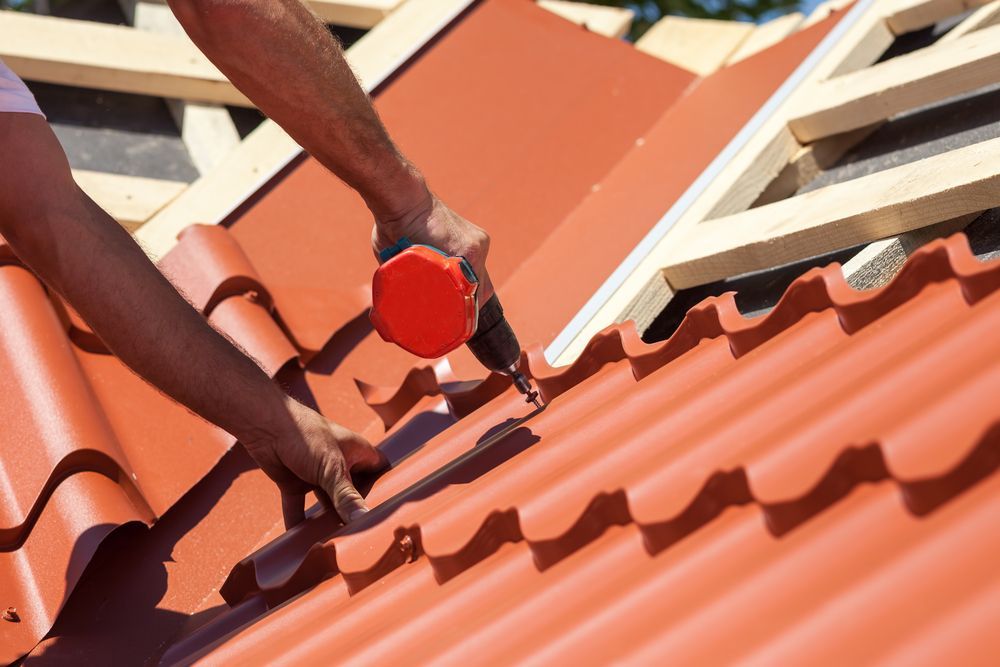 A Person Installing Red Roof Tiles With a Power Drill on a Sunny Day — Wilko Plate (Aust) Pty Ltd in Atherton, QLD