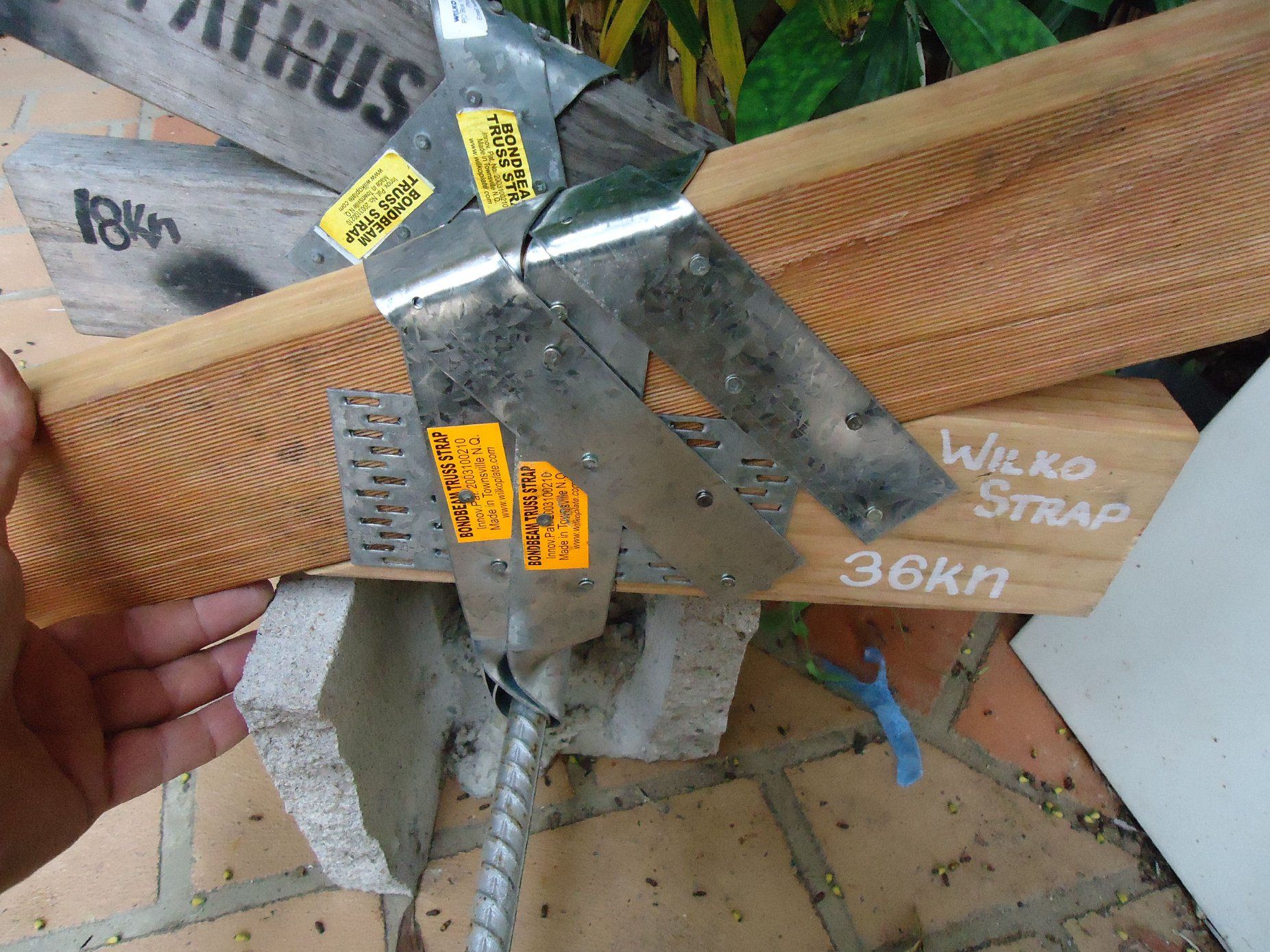Hand holding a wooden beam secured by a metal joist hanger with visible inspection stickers. — Wilko Plate (Aust) Pty Ltd in Annandale, QLD