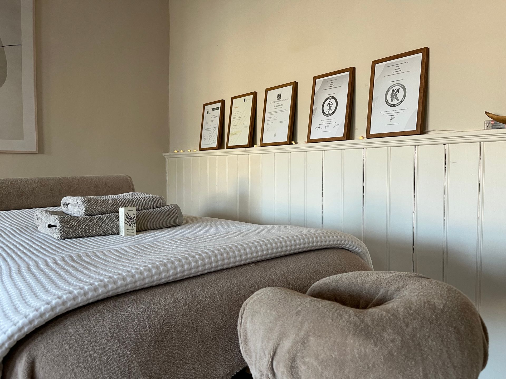 Gezellige slaapkamer met een bed, beige sierkussens en ingelijste prenten aan een witte lambrisering.