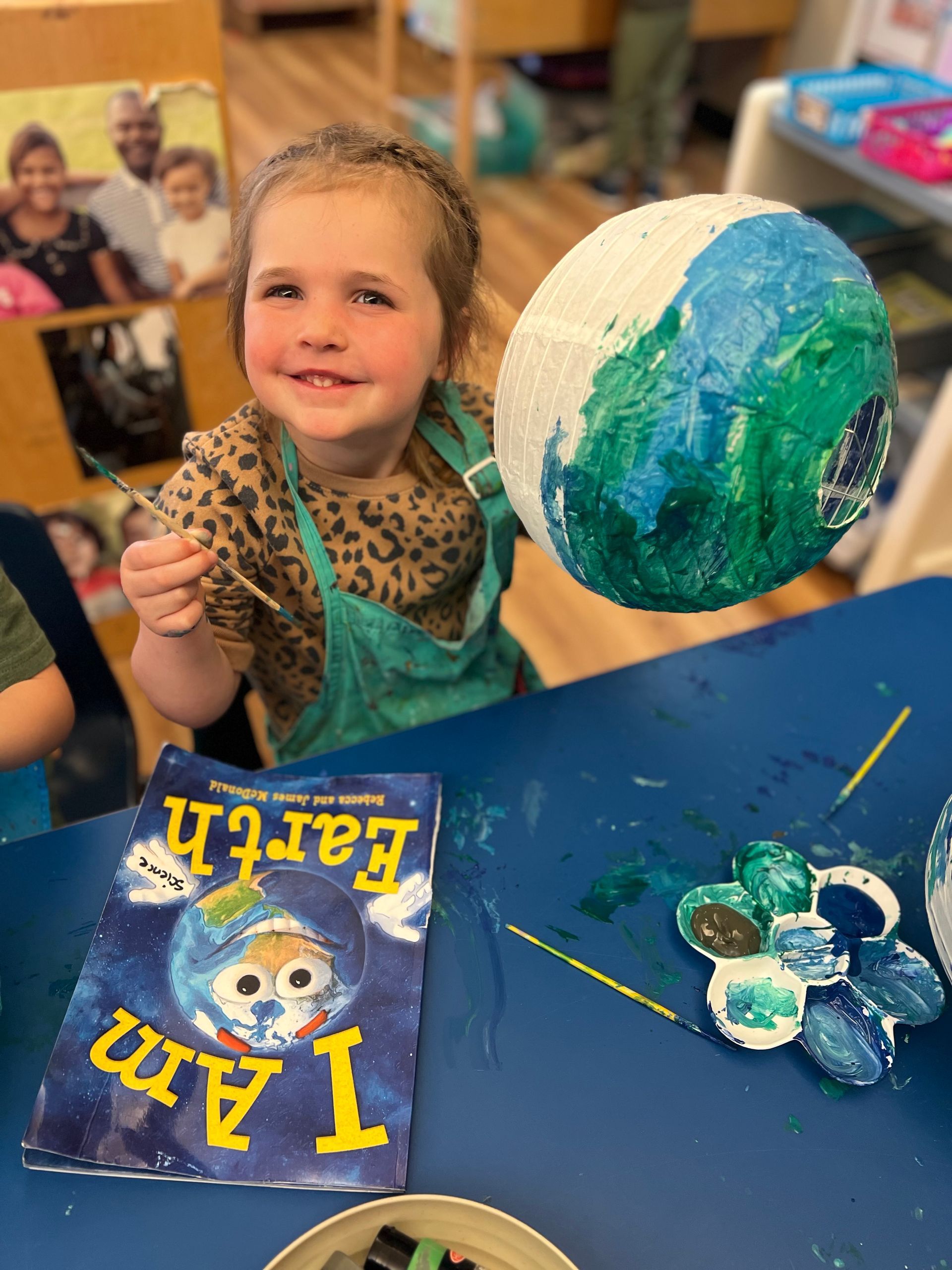 Child painting a blue-green globe craft at a table with paint and art supplies