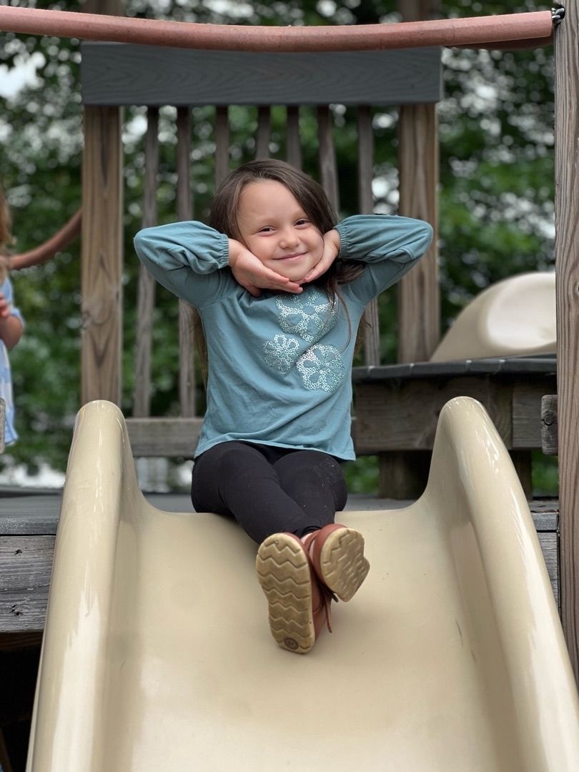 Child sitting at the top of a playground slide, smiling with hands behind head