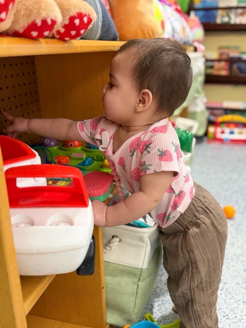 Toddler reaching for toys on a low store shelf beside a red-and-white bin