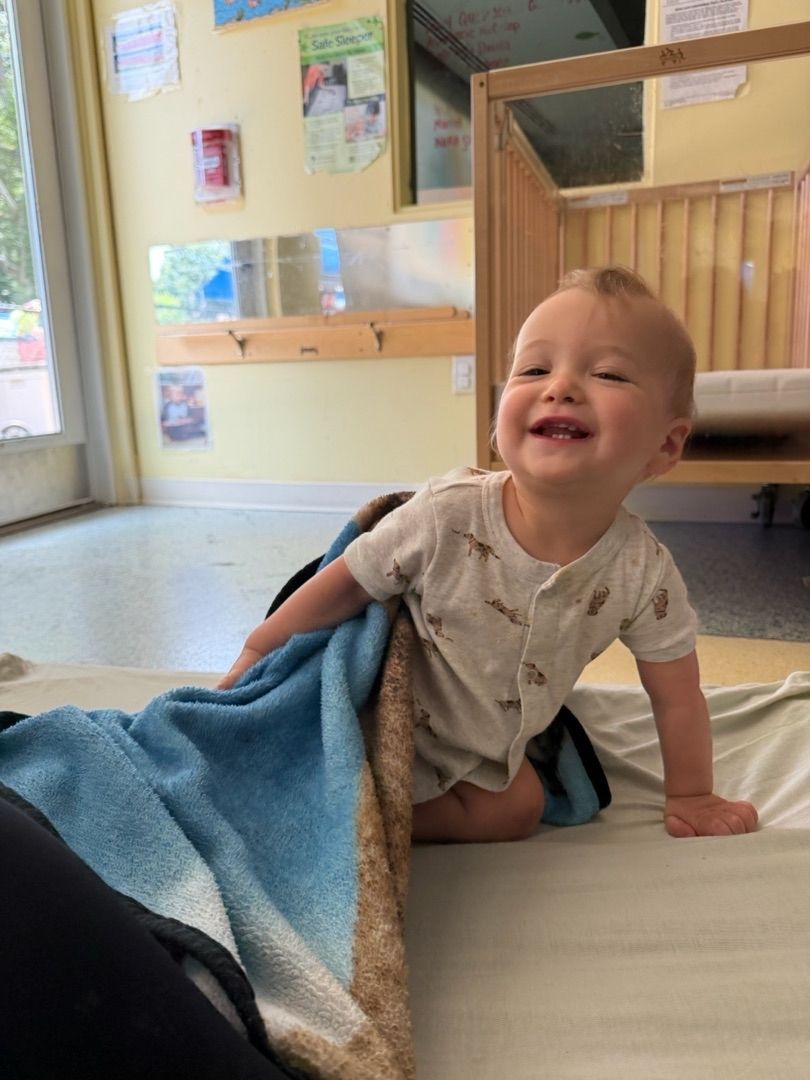 Smiling baby crawling on a light mat in a bright indoor playroom with a blue blanket.