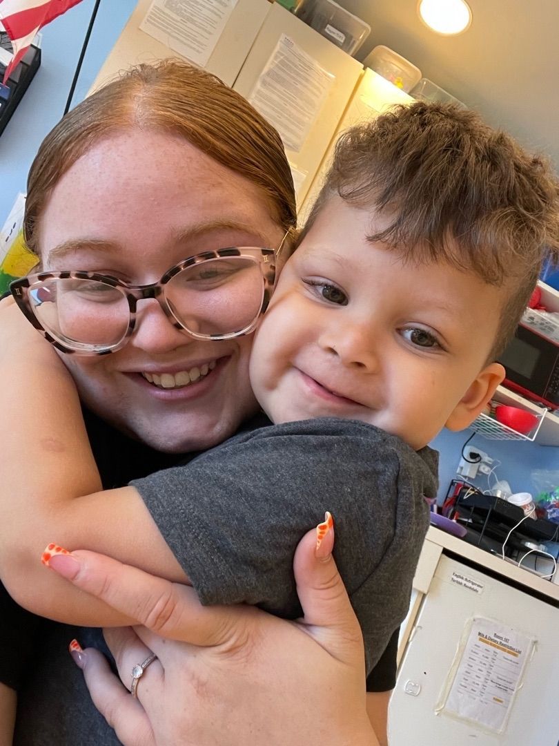 Smiling person hugging a toddler in a bright indoor setting