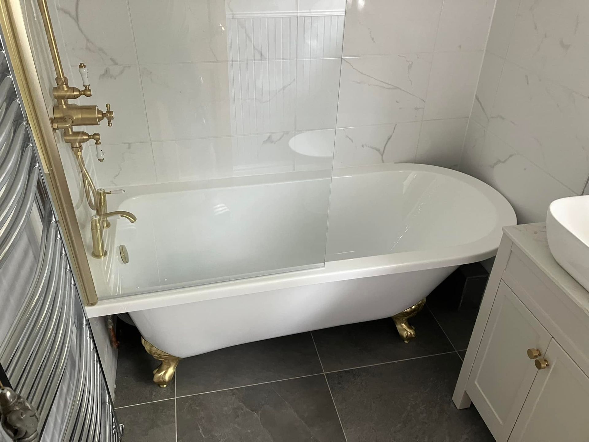 Bathroom with a white clawfoot tub, glass shower screen, brass fixtures, and gray tiled floor.