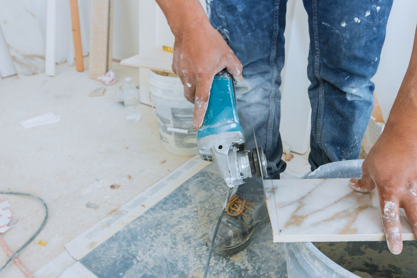 Person cutting tile with a power grinder, dusty interior setting.