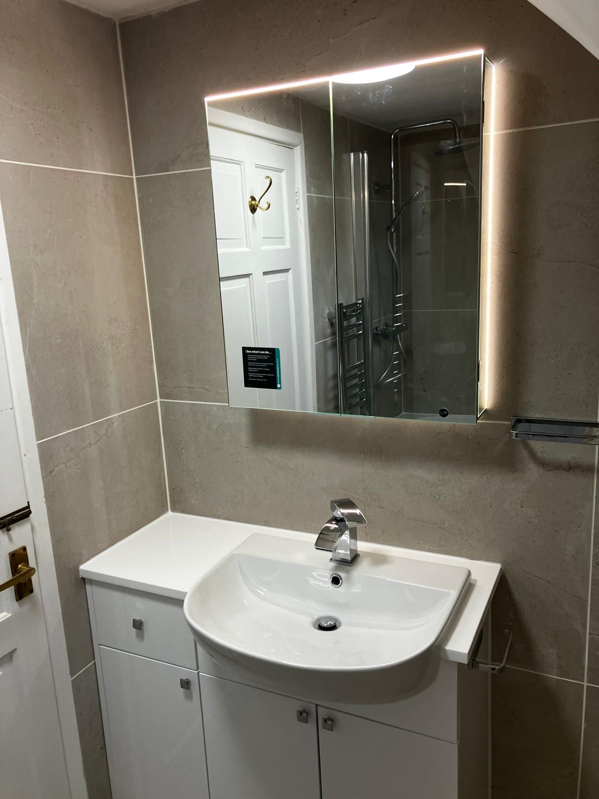 Bathroom with a sink, mirror with LED lighting, and white cabinets, tiled walls.