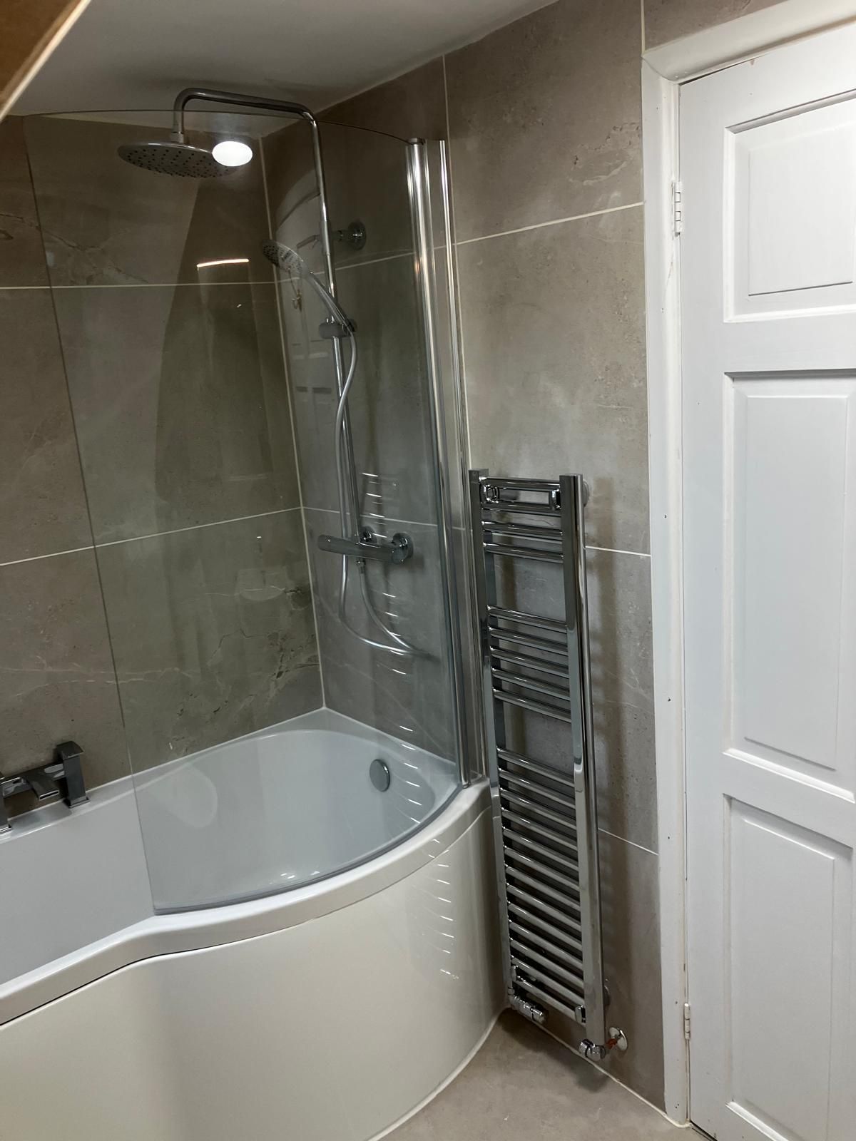 Bathroom with a white tub, shower, glass door, and silver towel rack. Cream-colored walls and a white door.