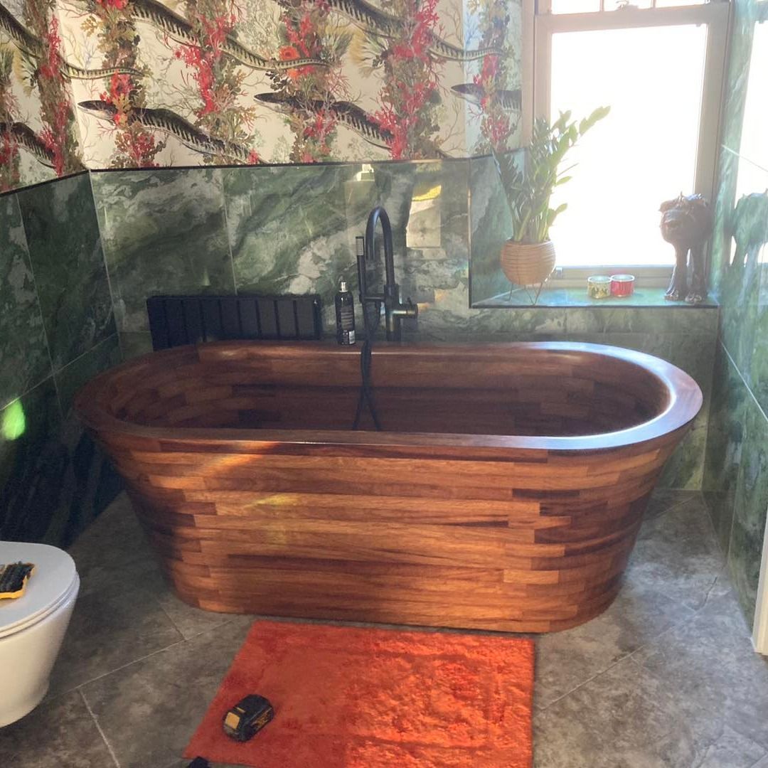Wooden soaking tub in a tiled bathroom with a bright window and orange rug