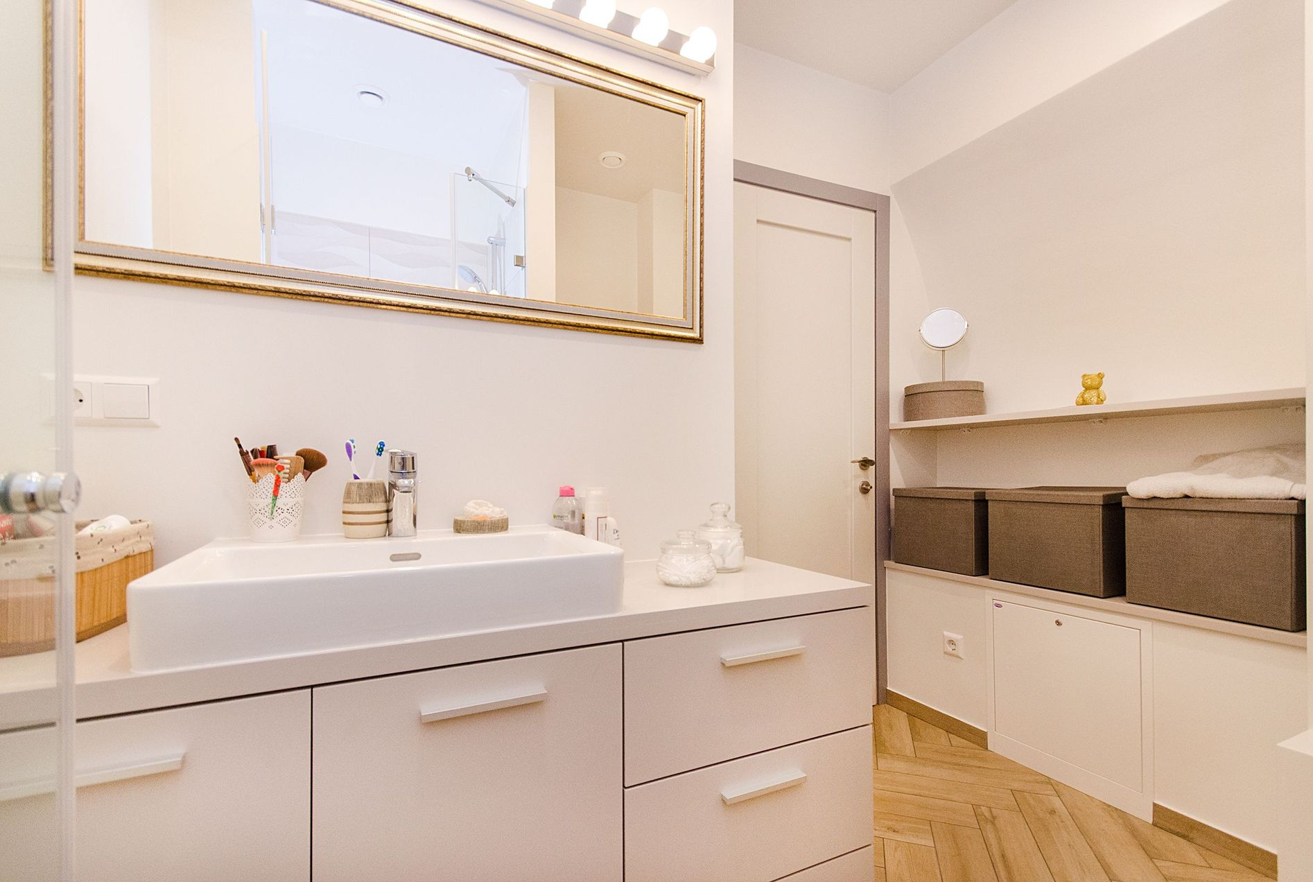 Bright modern bathroom with white vanity, large mirror, and woven storage baskets by the sink.