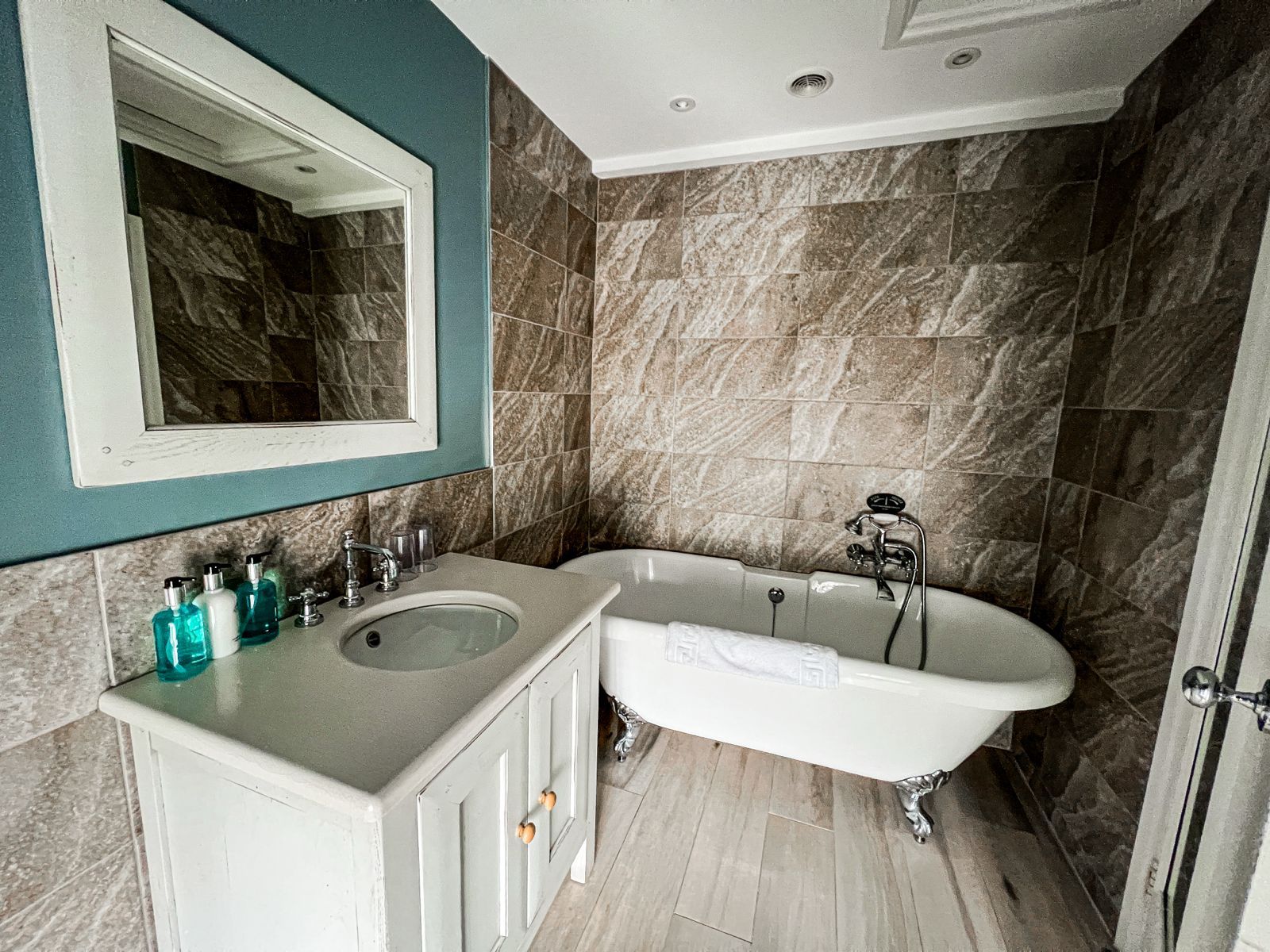 Modern bathroom with a freestanding tub, double vanity, large mirror, and stone tile walls.