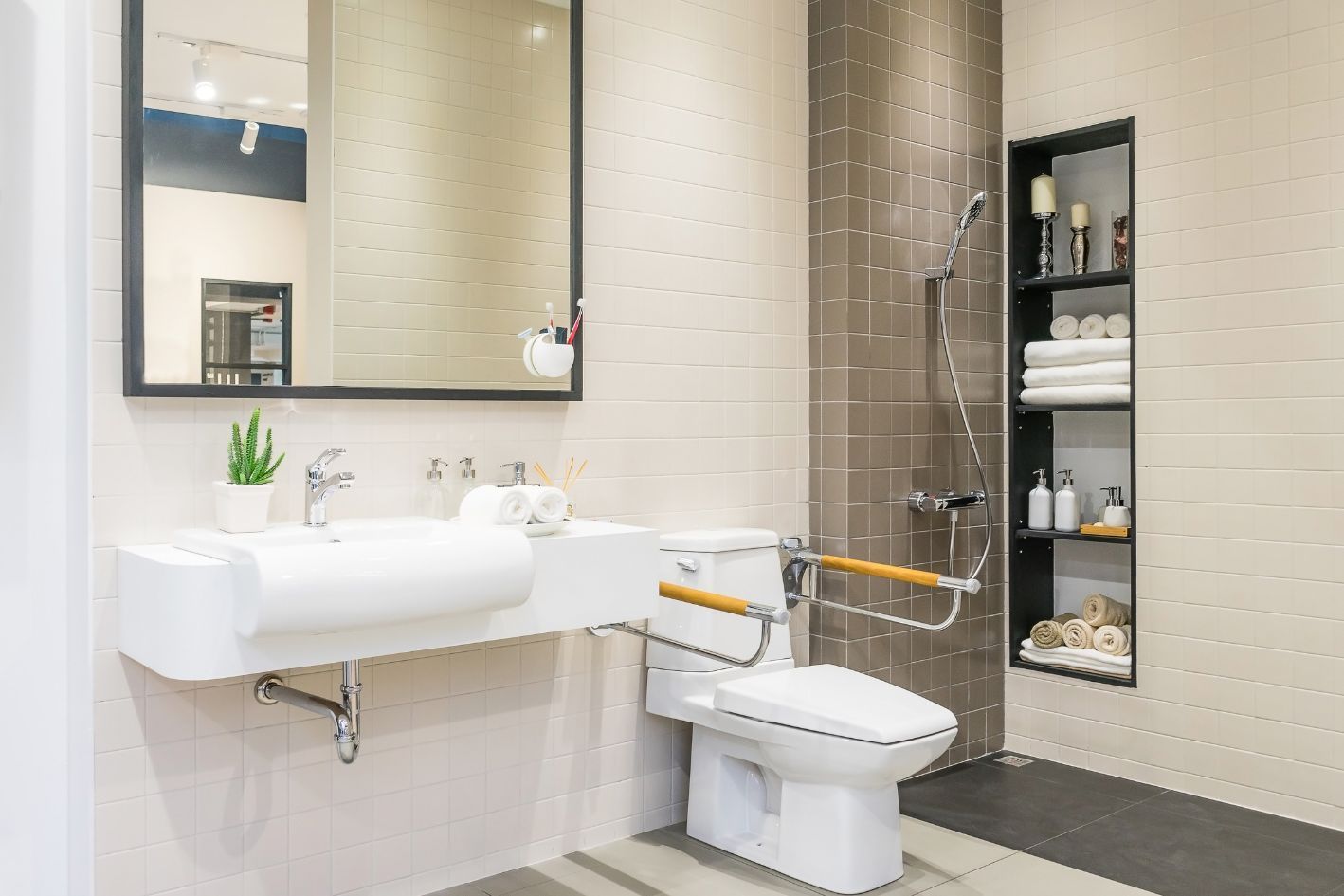 Accessible bathroom with sink, toilet with grab bar, and shower. Beige and gray tiled walls.