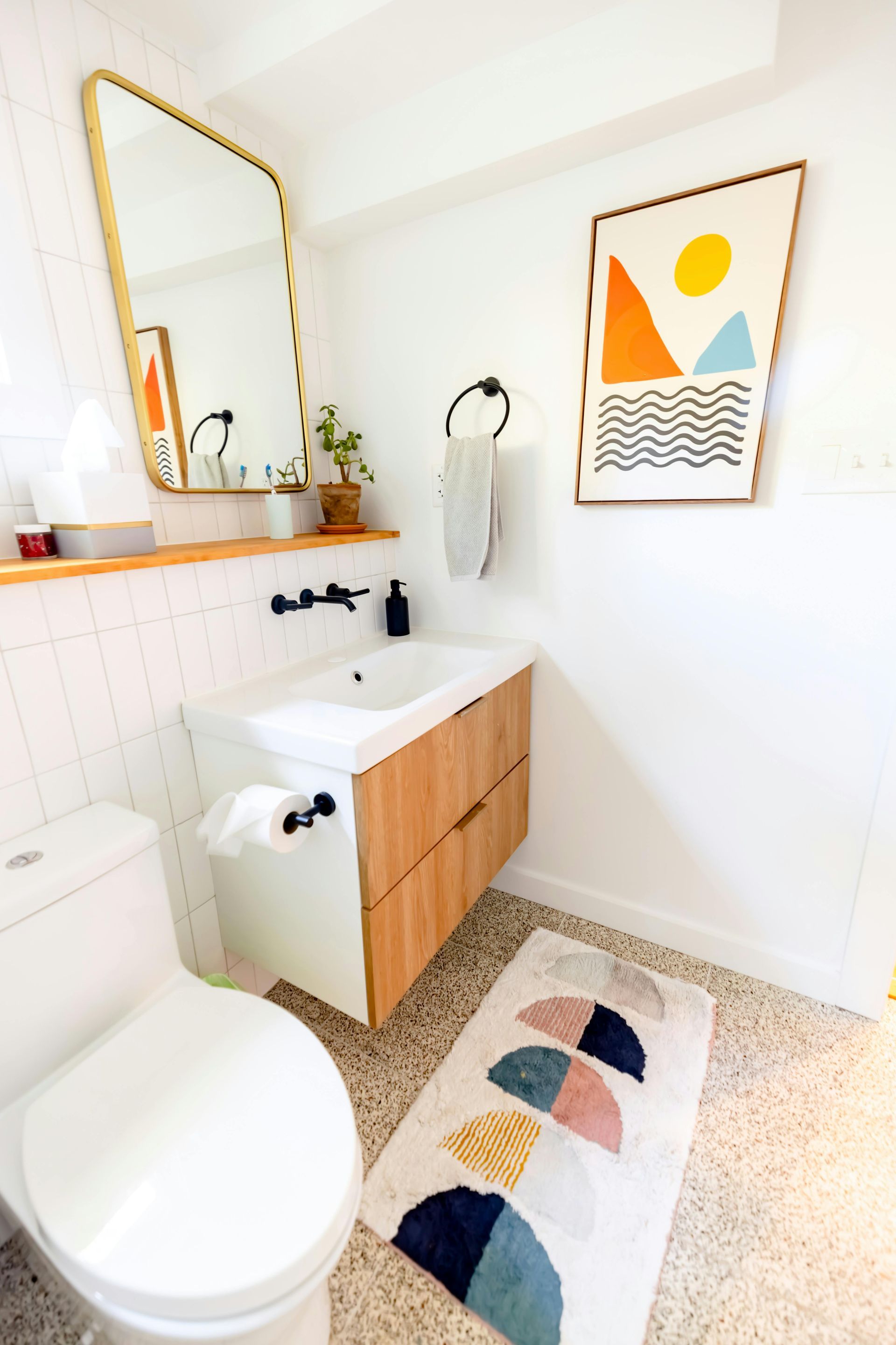 Small bathroom with a wooden vanity, art, a decorative rug, and white walls.